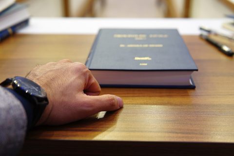 person holding black covered book on brown wooden table
