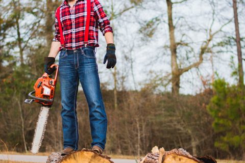 man holding chainsaw and standing on wood log