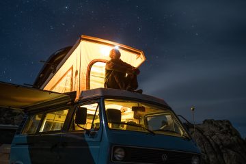 Off Road man sitting on top of blue van staring at sky during nighttime