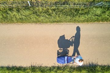 Stroller man in black jacket and blue denim jeans sitting on gray concrete road during daytime