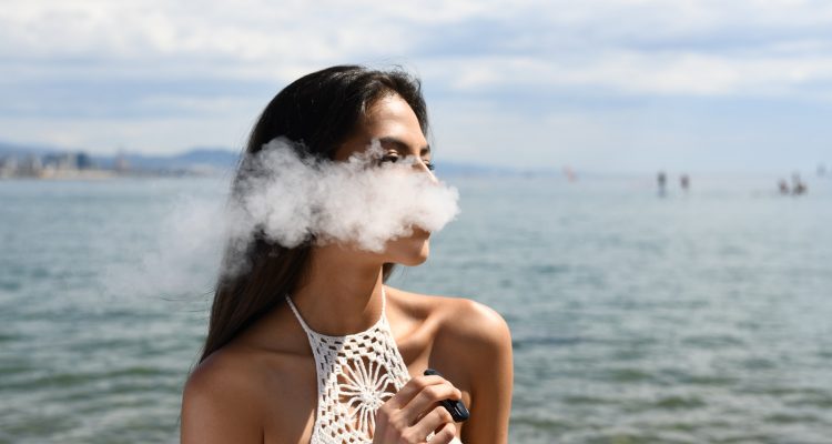 510-thread battery Vape Juice Vaping woman wearing white sleeveless top smoking tobacco while standing near blue sea under white and blue skies during daytime