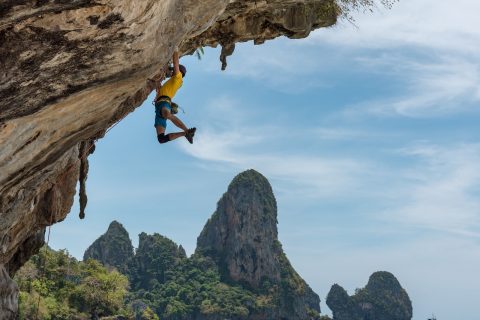 physical activities man climbing cliff beside beach