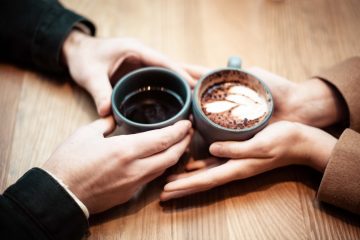 date two person holding ceramic mugs with coffee
