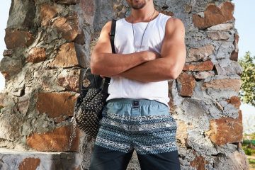 Relax menswear man in white tank top and black and white plaid shorts standing beside brown rock