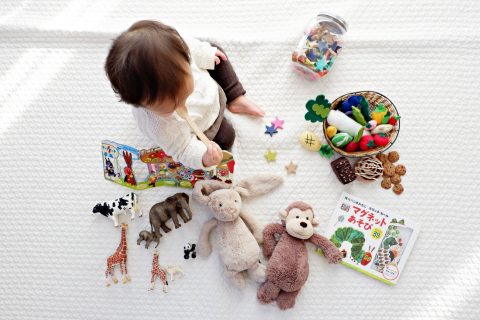 toddlers boy sitting on white cloth surrounded by toys