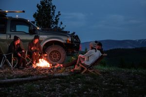Overlanding 4x4 Off-Road Truck man in white shirt sitting on brown wooden chair near black suv during night time