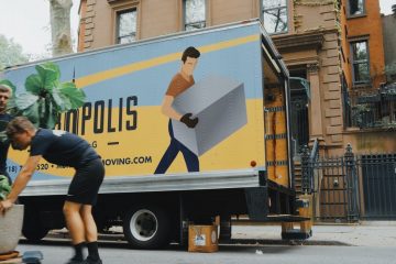 Moving woman in blue shorts and black boots standing beside yellow and white truck during daytime