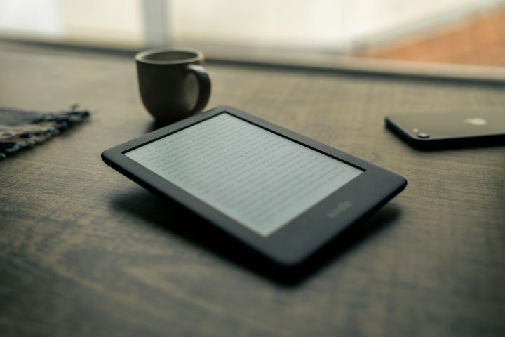 Connected Kindle black android smartphone beside black ceramic mug on brown wooden table