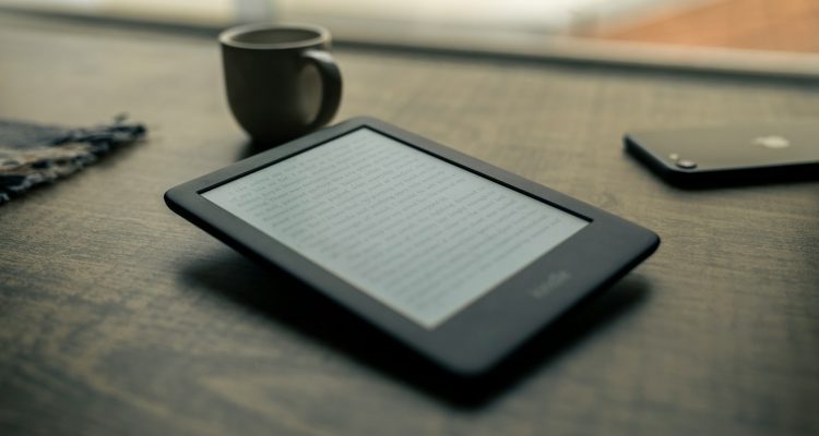 Connected Kindle black android smartphone beside black ceramic mug on brown wooden table