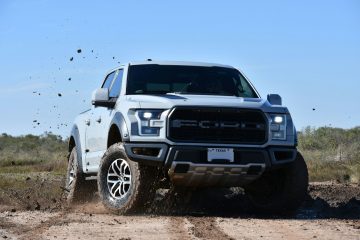 Raptor a white truck is driving through the mud