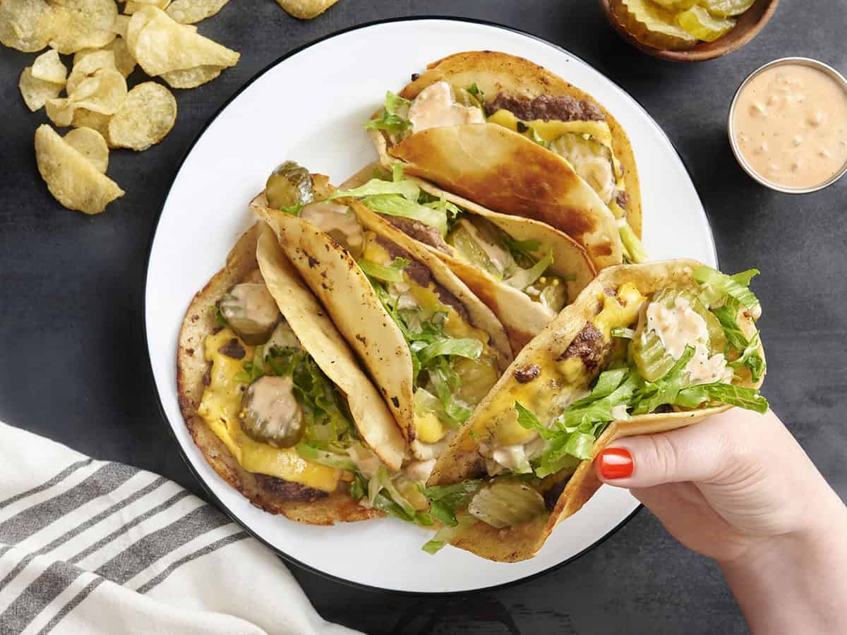 Hand holding a smash burger taco with melted cheese and toppings