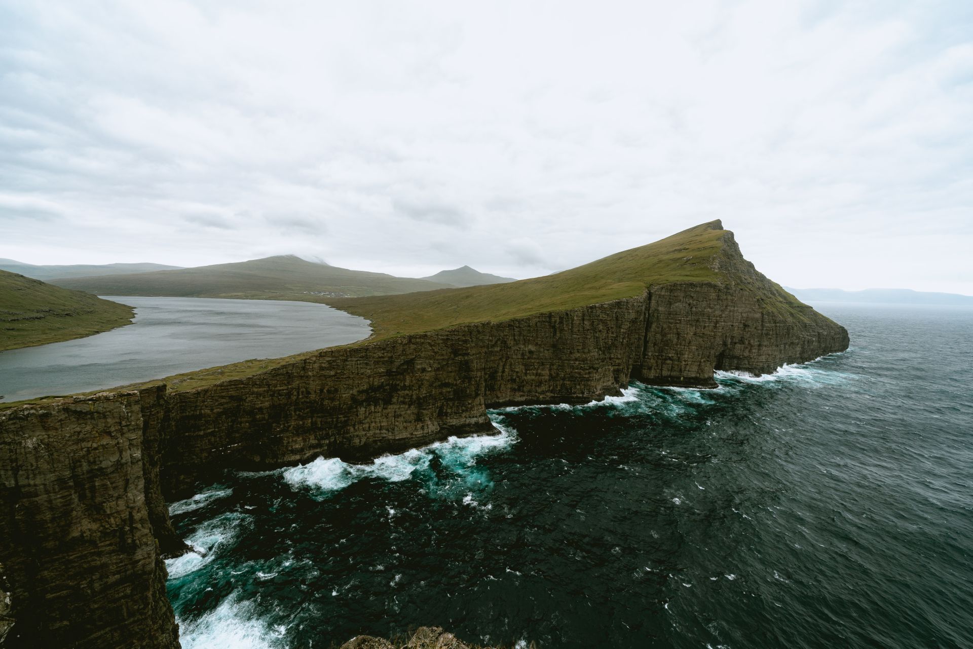 Dramatic view of the Faroe Islands cliffs meeting the vast ocean under a cloudy sky