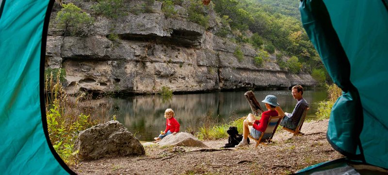 Visitors relax beside a limestone bluff and clear pond along the Sabinal River at Lost Maples State Natural Area in Texas