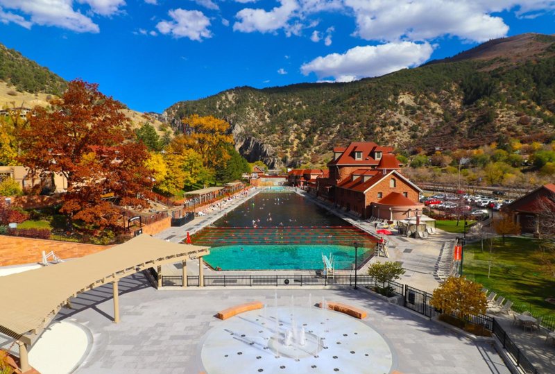 The large outdoor hot springs pool at Glenwood Hot Springs Resort with autumn trees and mountains behind it