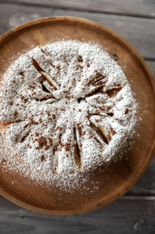Round apple cake dusted with powdered sugar on a wooden board