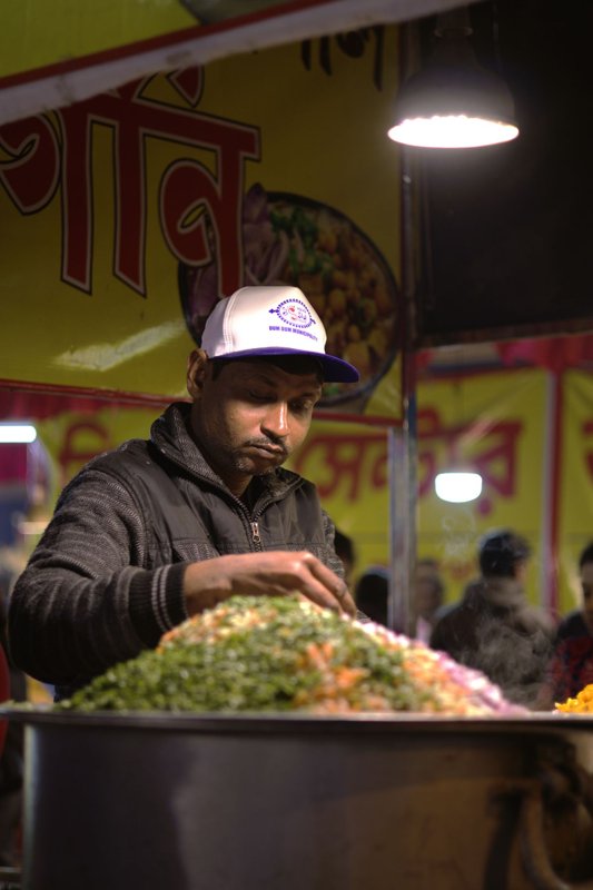 A street food vendor cooking under lights at a night market