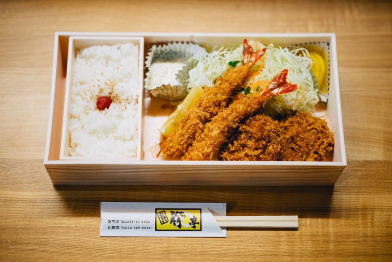 A Japanese bento box with rice, fried shrimp, and cutlet on a wooden table