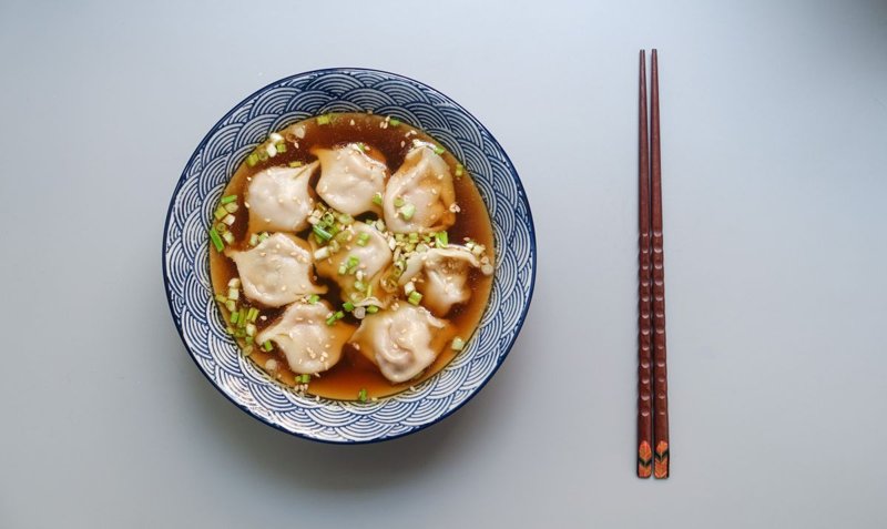 Bowl of dumplings in clear broth with scallions and chopsticks